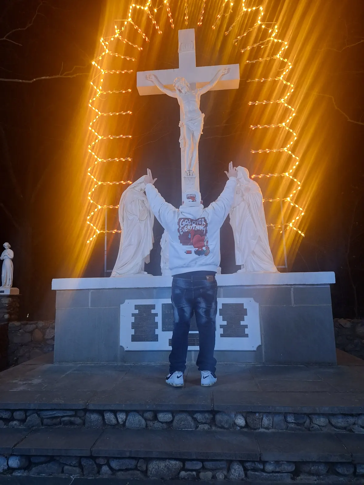 Keith, founder of NVUS Hearts, arms raised before a lit cross